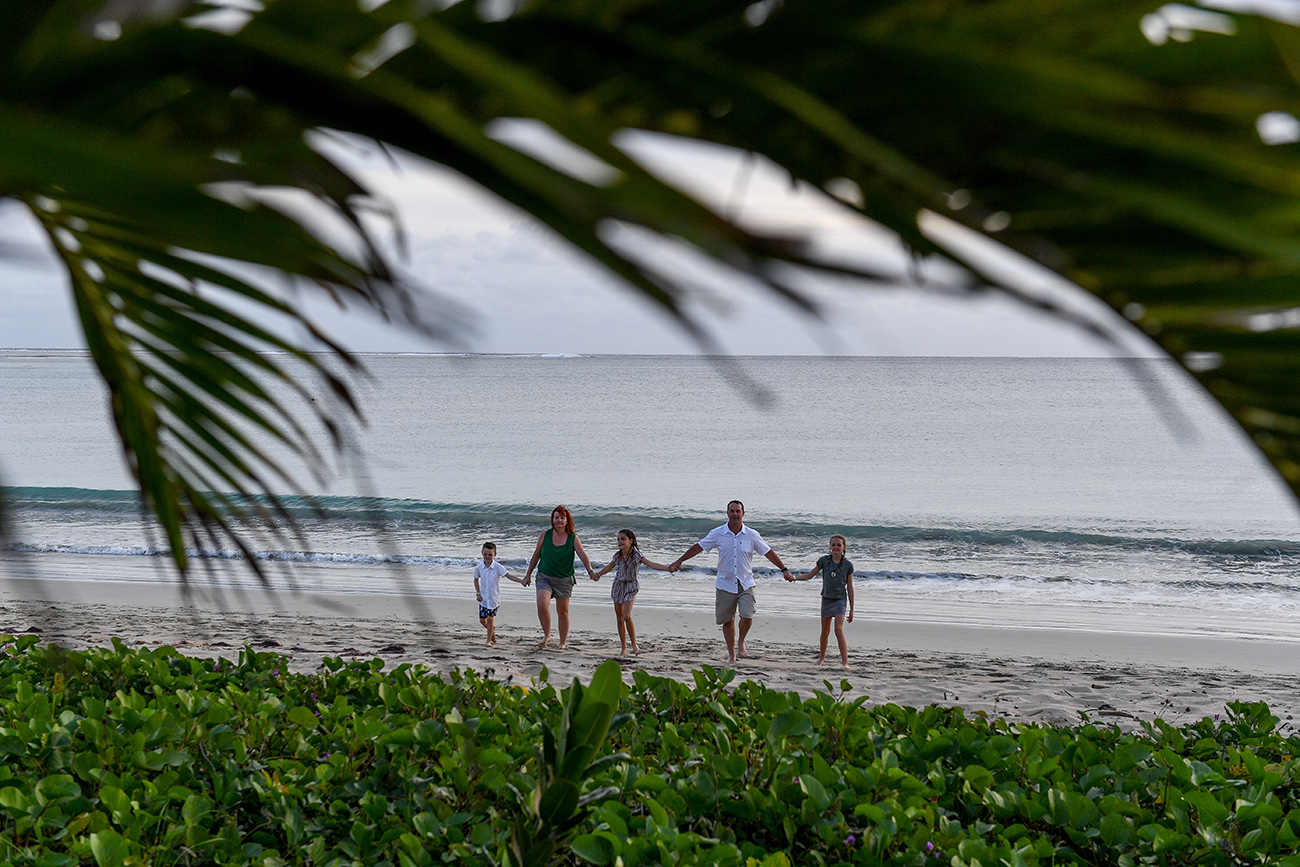 Wide shot through palm trees of family strolling in the beach in Fiji