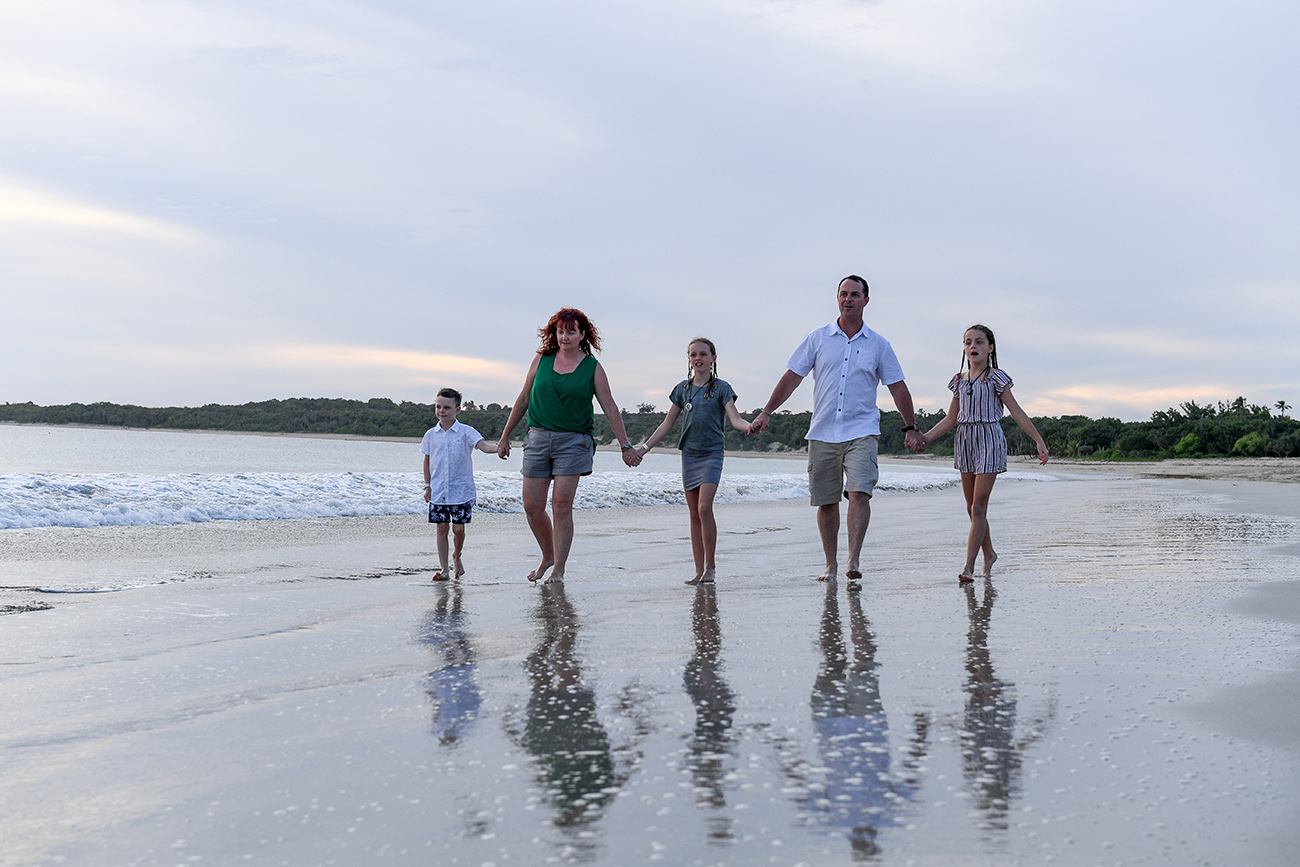 Cute family hold hands as they walk on the beach against Fiji ocean and sunset