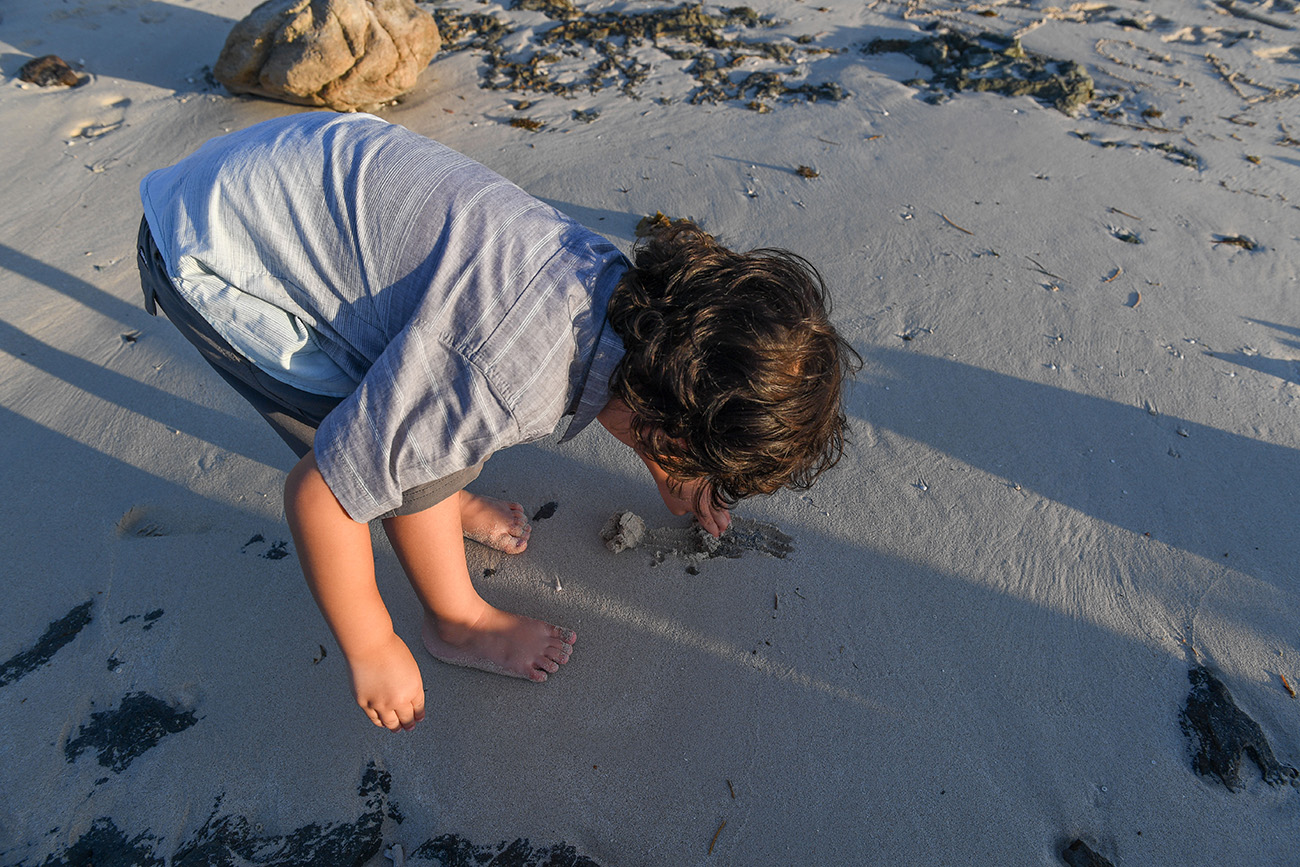 Cute little boy picks up rocks on the dark sand in Fiji