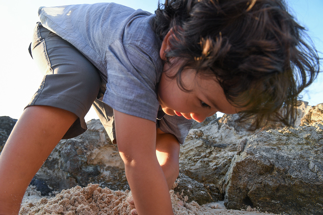 Cute curly haired boy picks seashells in Malolo Fiji