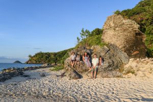 Wideshot of family seated on large boulder in family photo session in Fiji