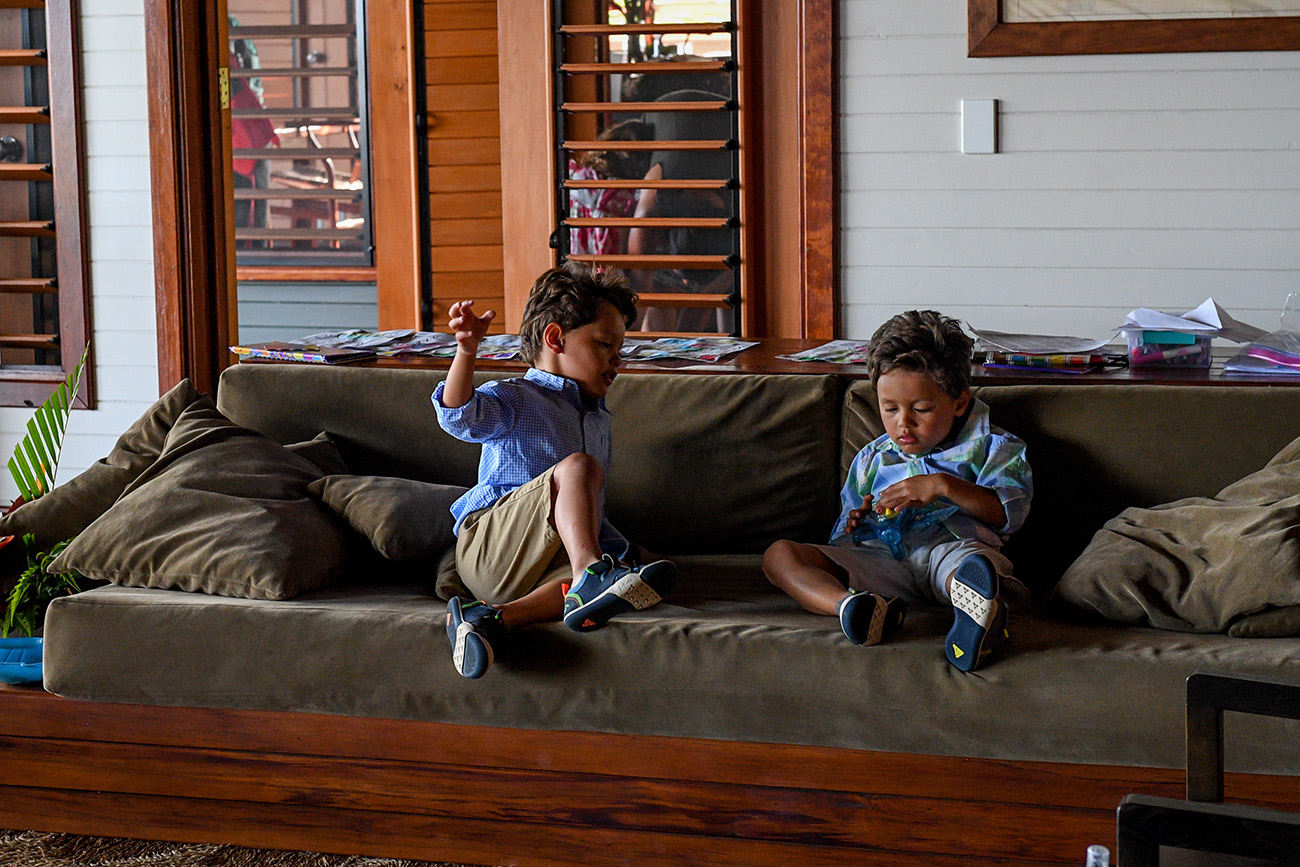 Triplet boys seated on couch indoors during family vacation in Fiji