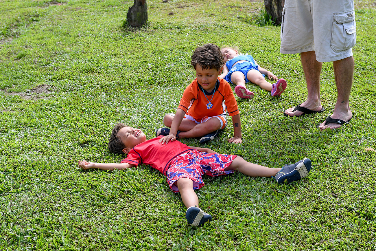 Cute Triplets play in grass during Fiji family vacation