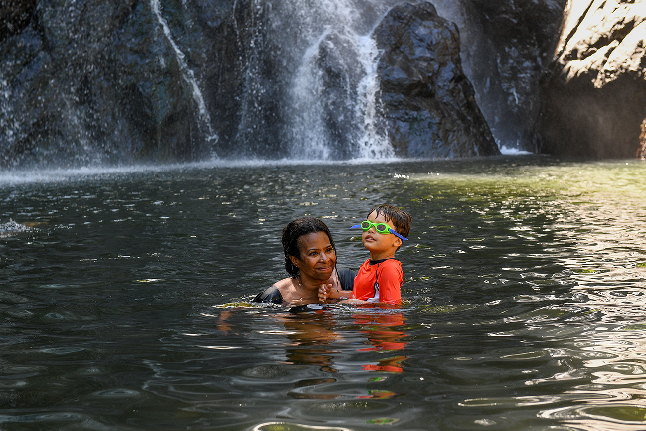 Mom and son swim in the river against the waterfall in Fiji
