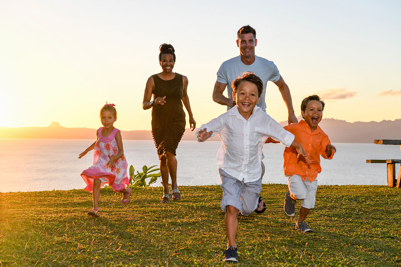 Family runs against ocean and sunset in Fiji family photo shoot