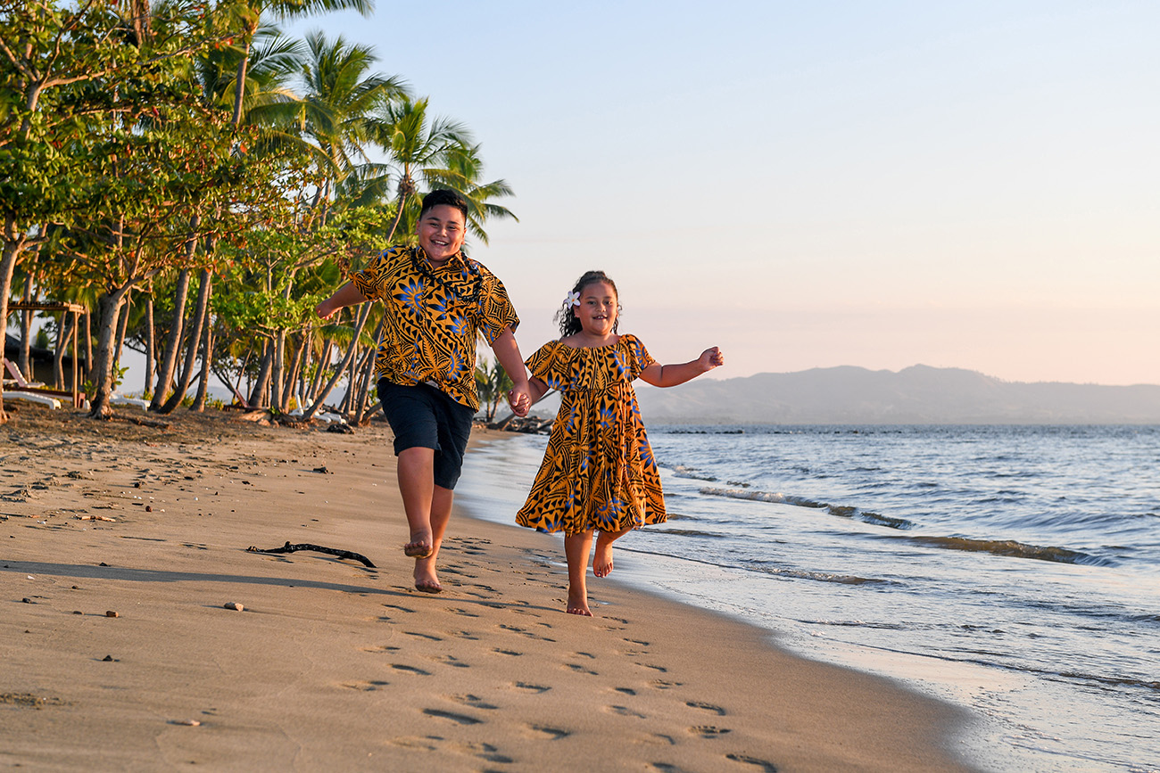 Brother and sister run and play along the shore at Double Tree Hilton Fiji
