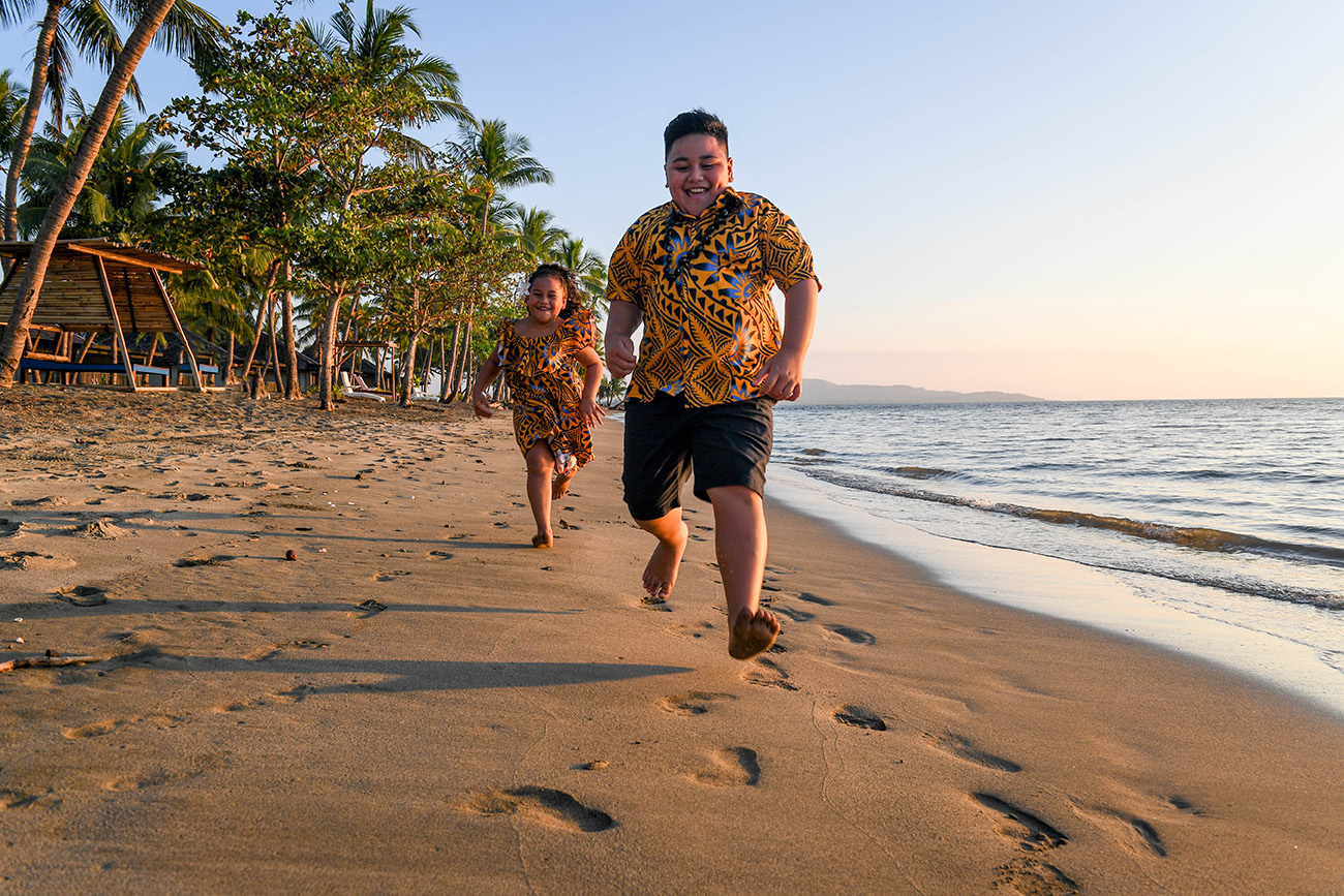Brother and sister run and play on the beach at Double Tree Hilton Fiji