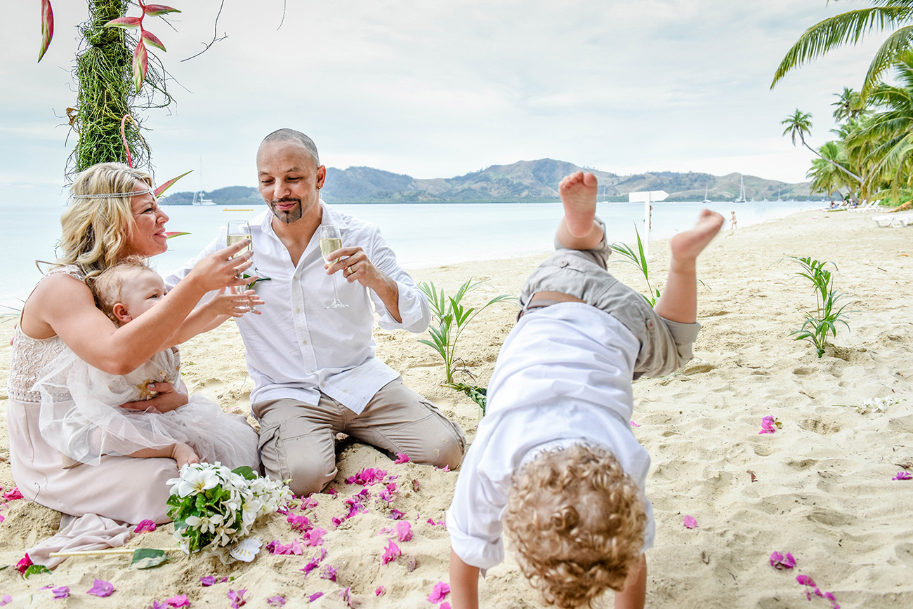 Newly married couple drink champagne as their children play in the sand