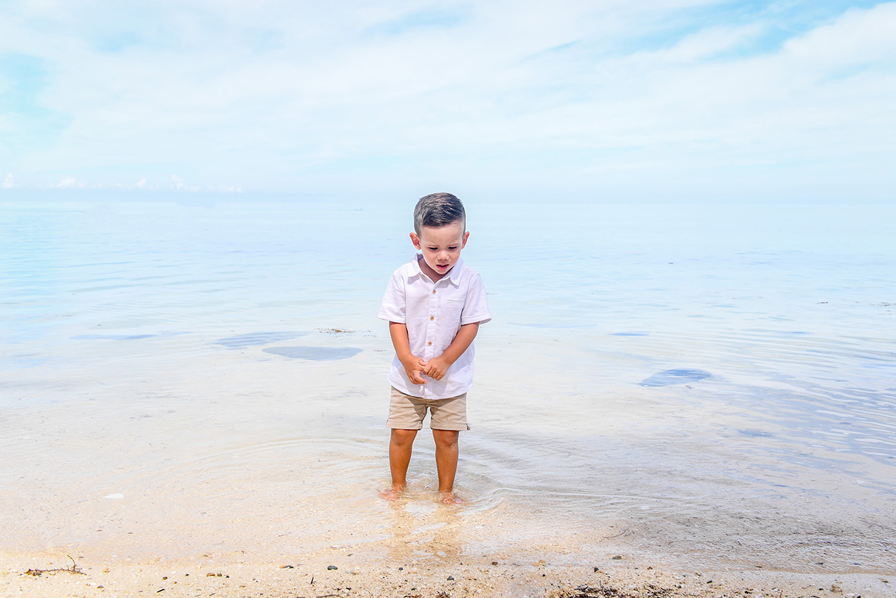 Cute baby boy watching fish in clear Fiji sea against stunning baby blue sky