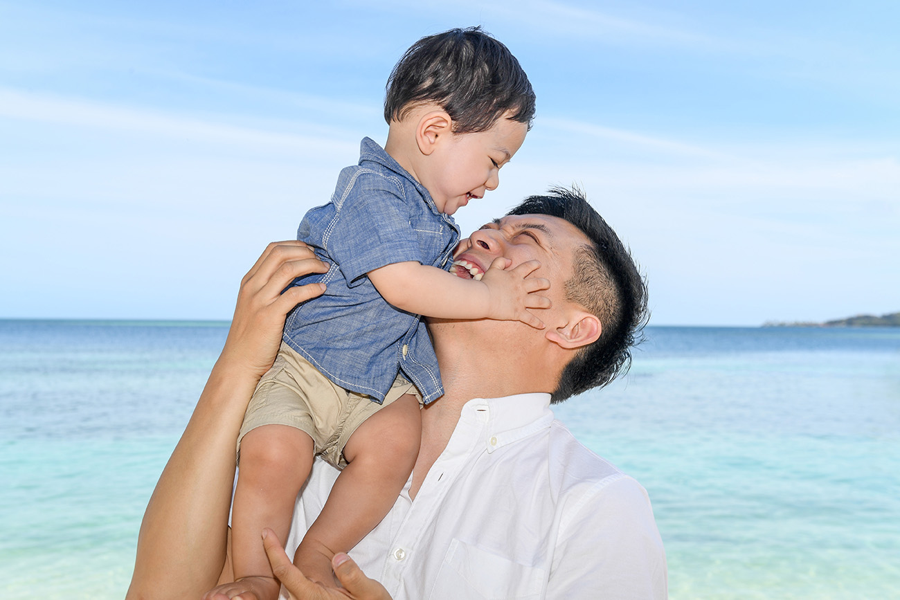 The father lifts his son above his head while in the turquoise blue waters