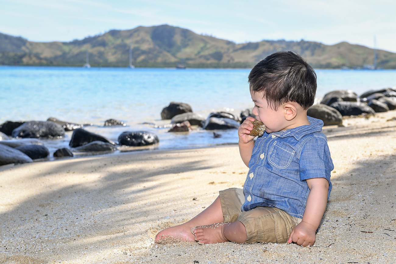The cute little boy puts the coral rock in his mouth at Plantation Island Resort Fiji