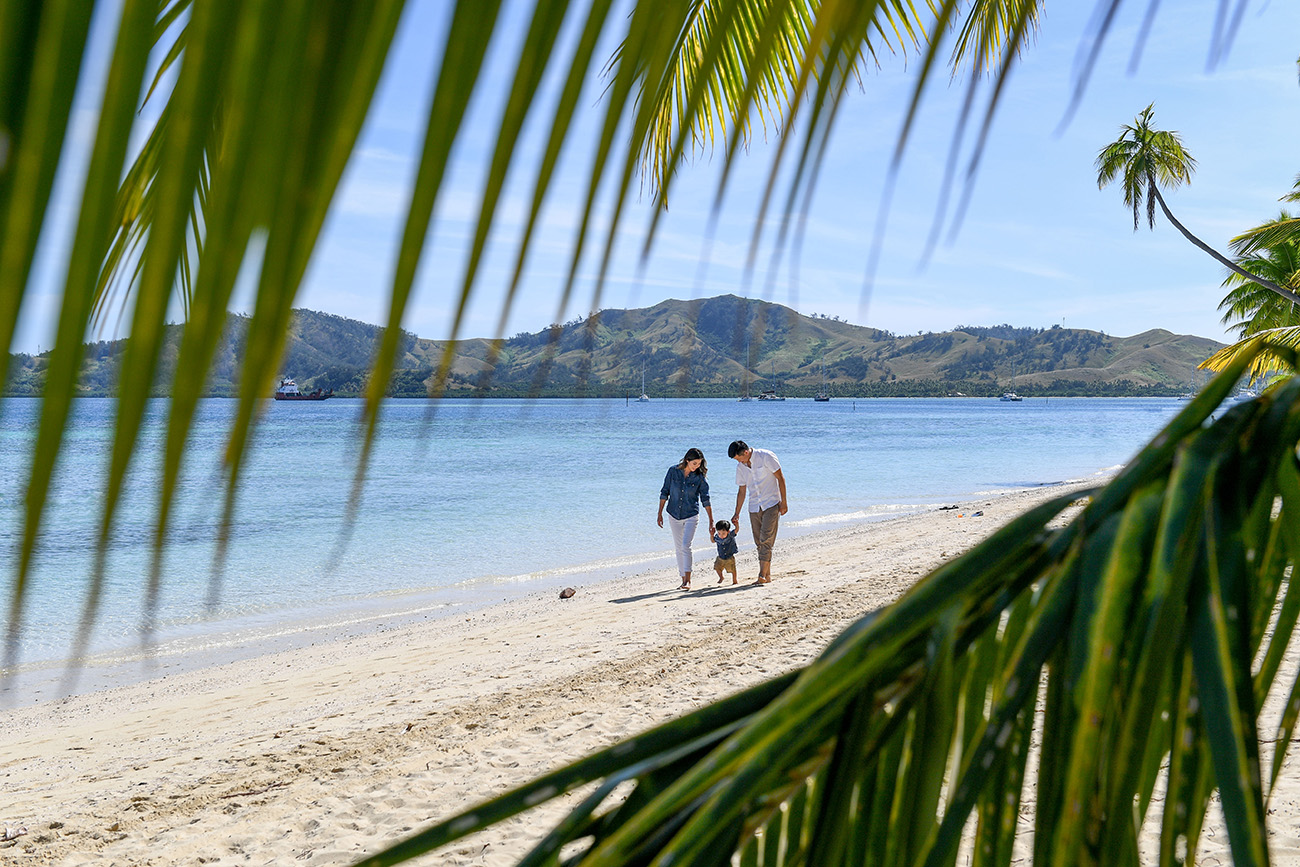 Palm tree fronds frame the couple as they have a stroll on the beach at Plantation Island Resort Fiji