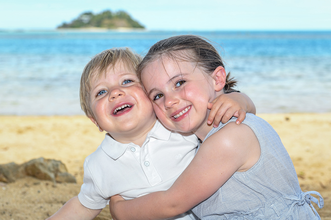 The sister hugs her cute little brother while seated on the warm sandy beaches at Malolo Island