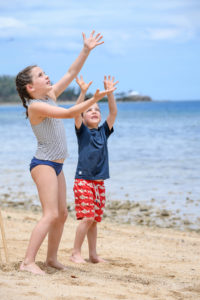 The cute babies reach for the cricket ball in the air while playing beach cricket