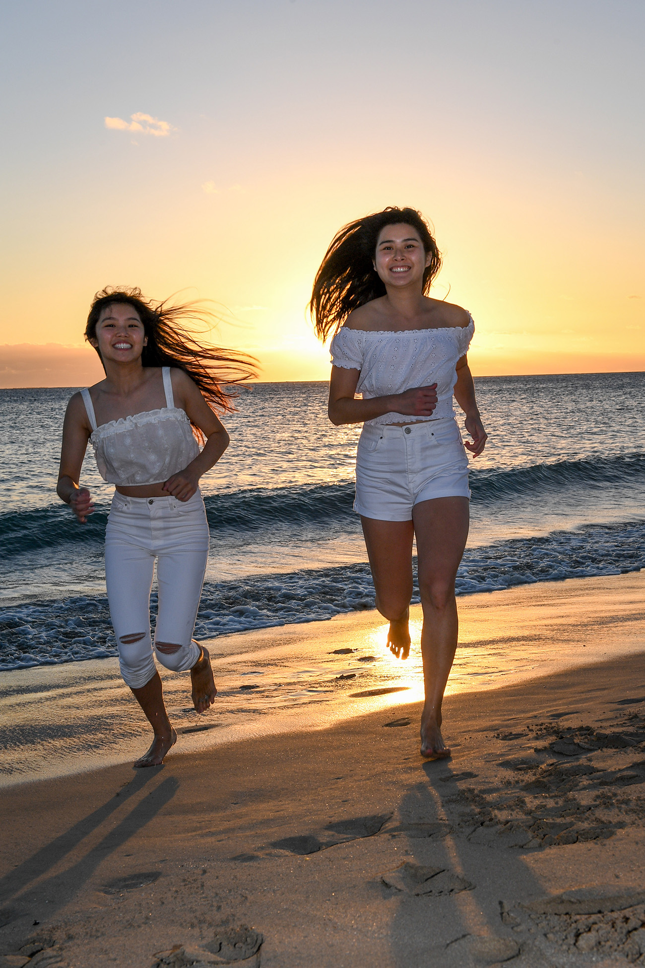 Asian sisters run on the beach against the setting Fiji sun