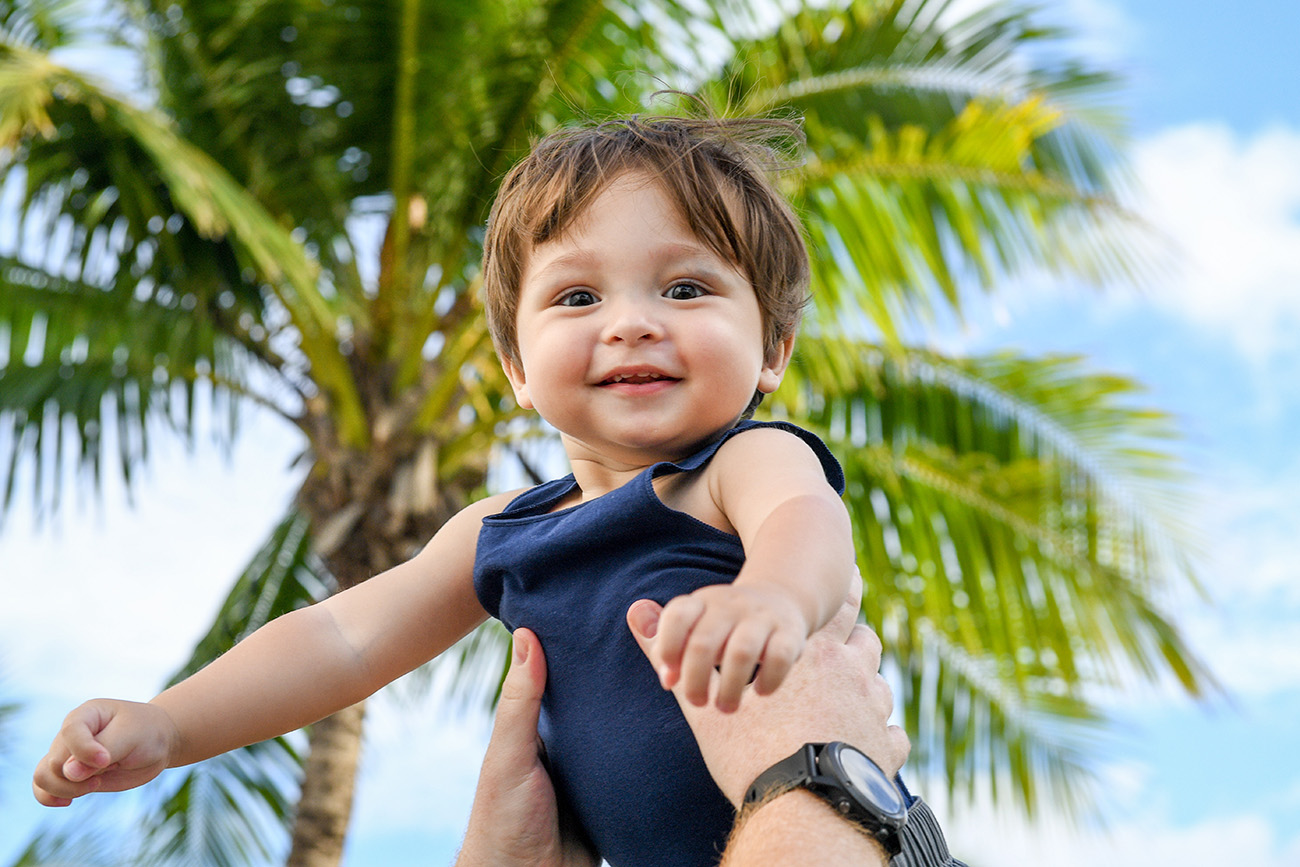 A cute caucasian baby is lifted up against a palm tree