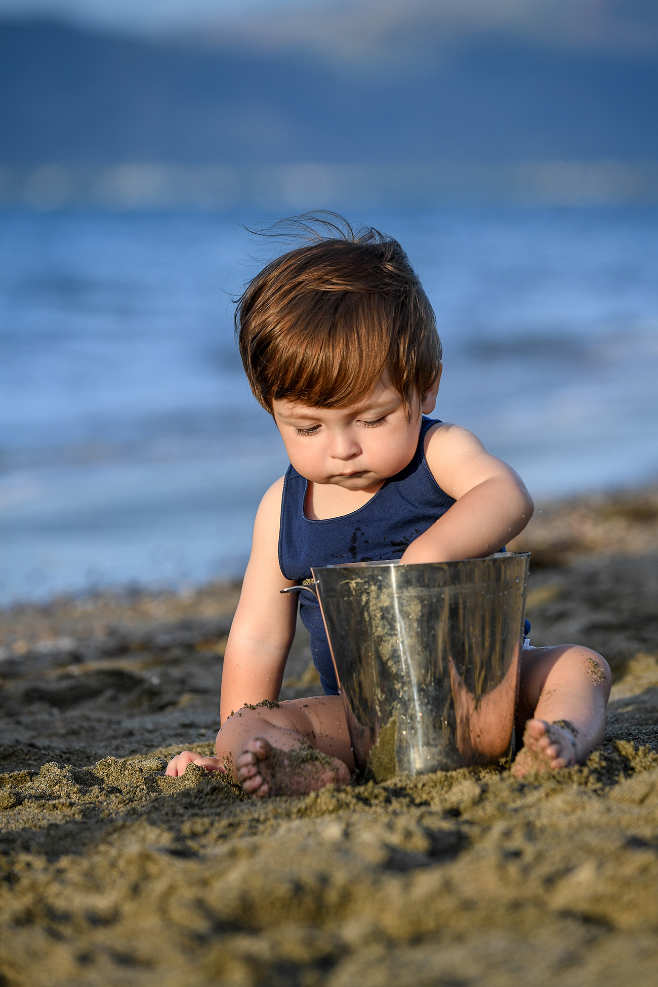 A baby plays around with sand in a bucket at the beach