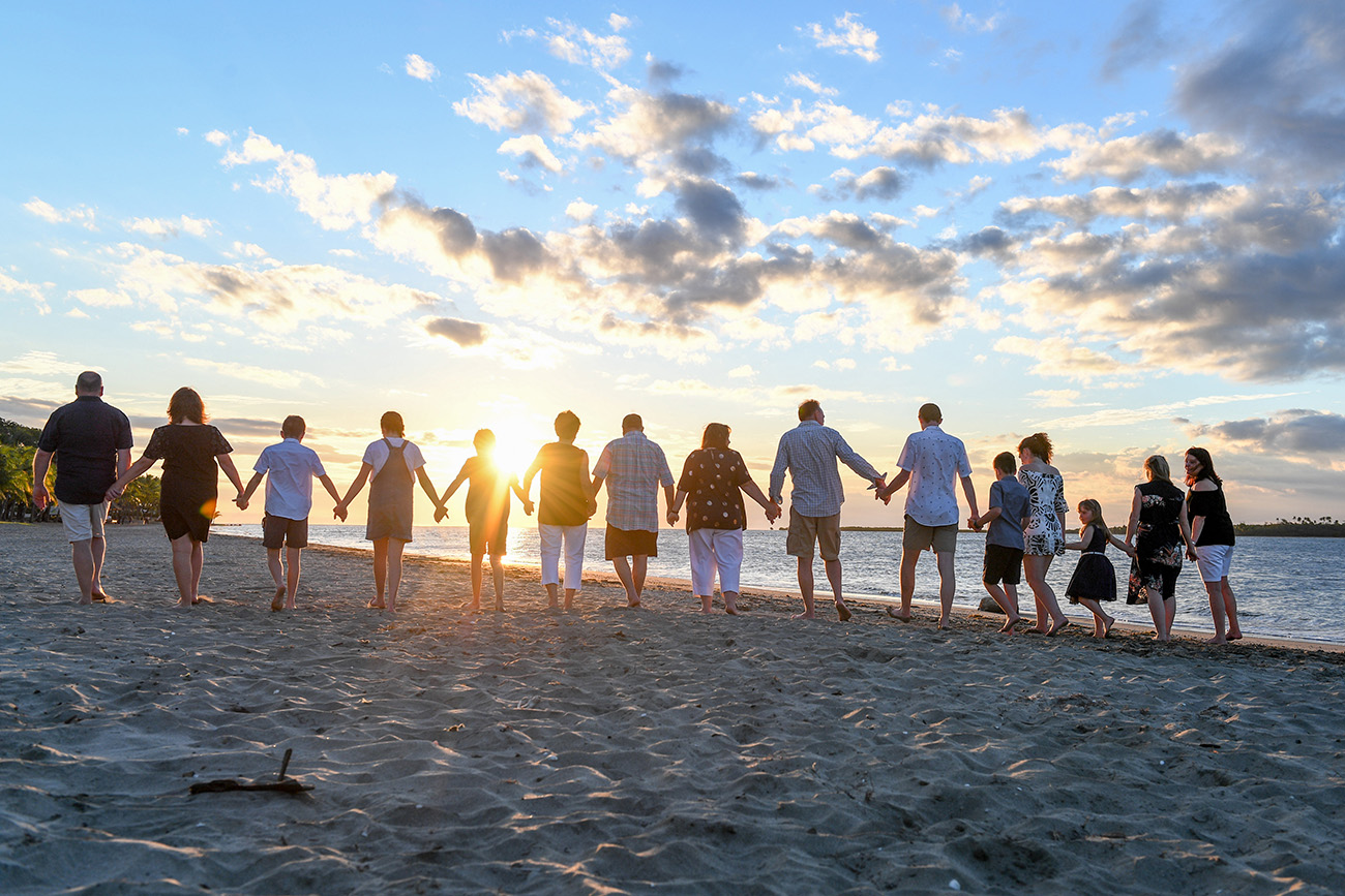 Extended family members hold hands as they walk towards the sunset at Natadola beach