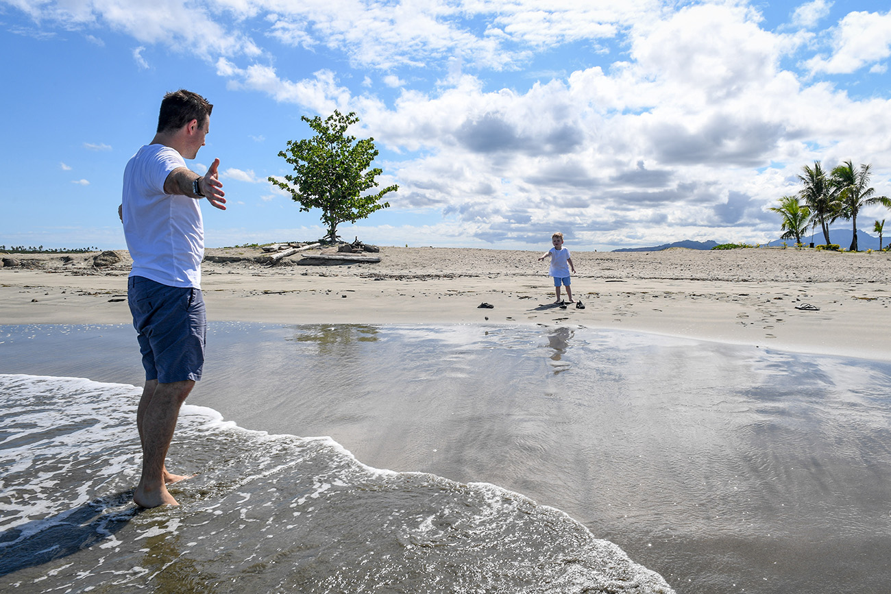 A father waits with open arms for his son while standing on the beach