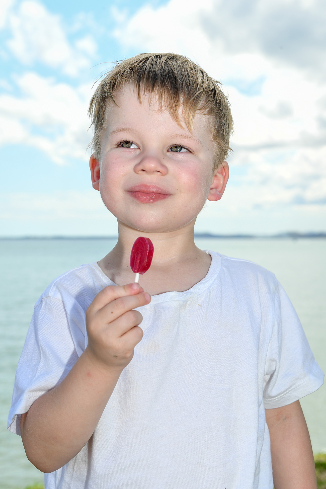 A blonde boy meditates while licking a lollie at the beach