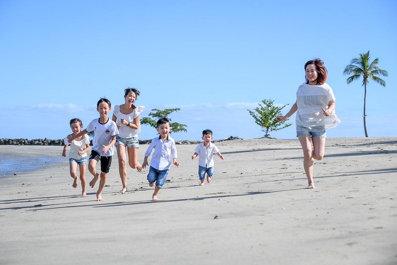 Two families run on the beach against baby blue sky