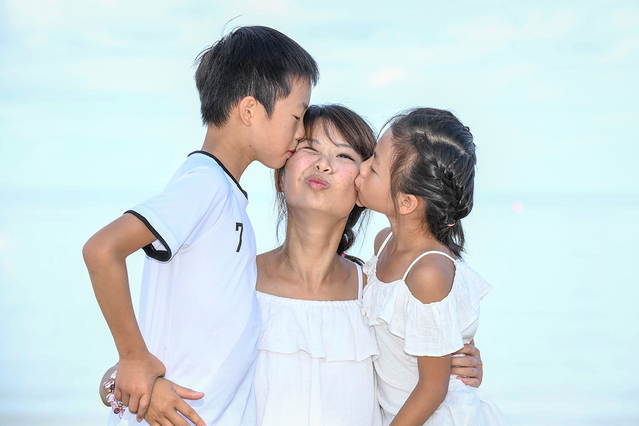 Asian daughter and son kiss their mother against baby blue sky