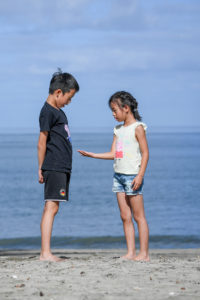 A sister shows her brother a shell she picked on the beach