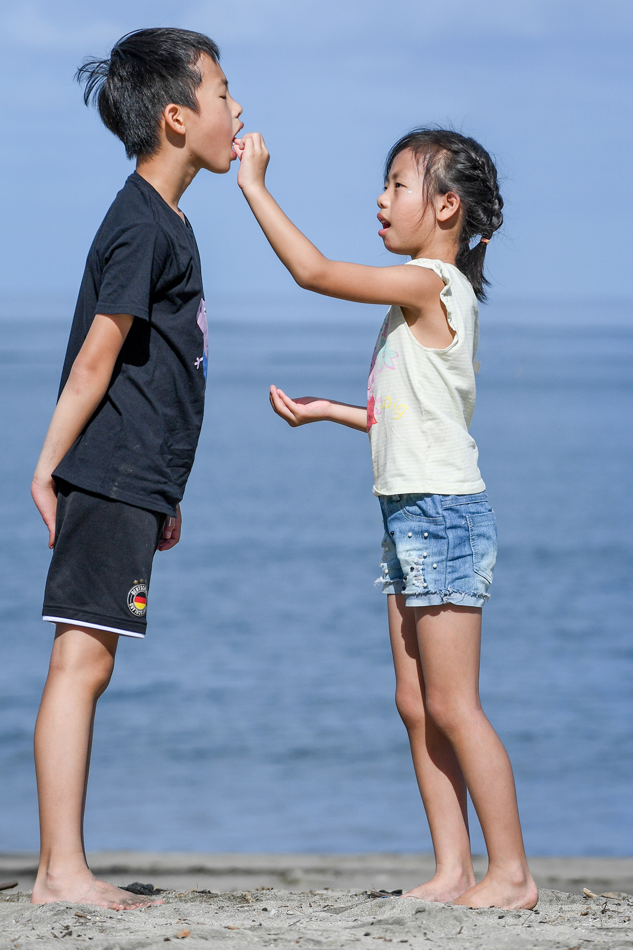 A sister feeds her brother with the Pacific ocean in the background