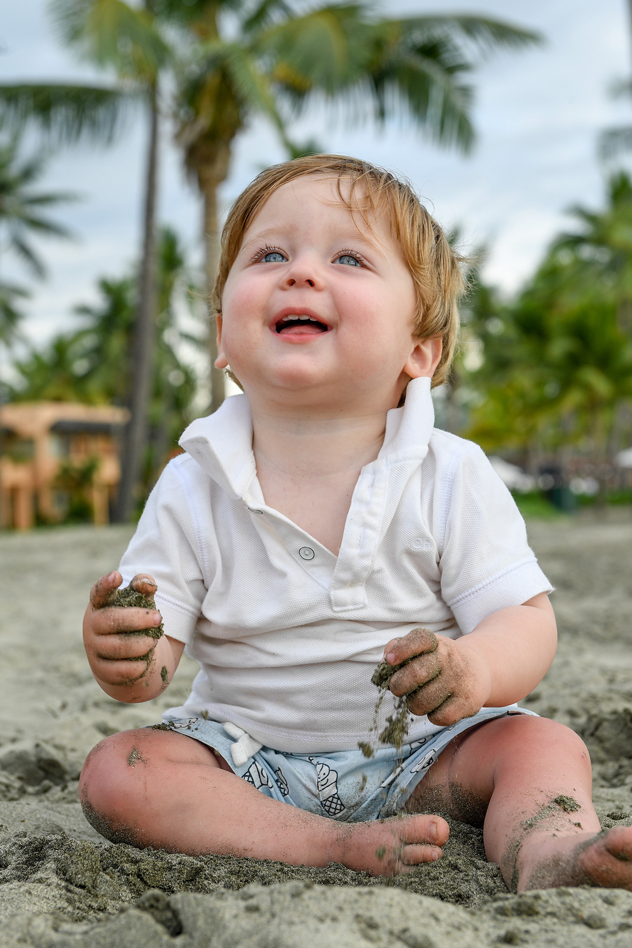 A baby gets his hands dirty while seated on the beach