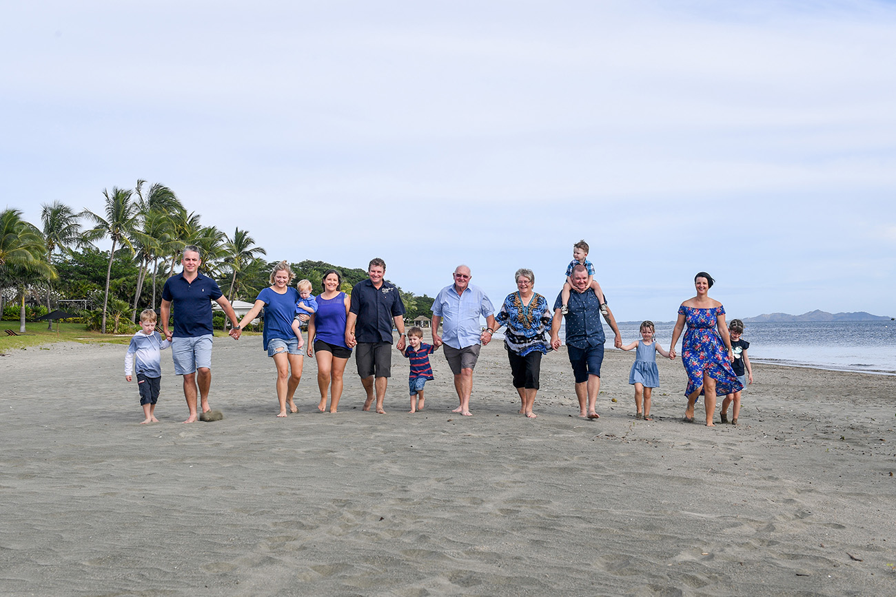 An extended family holds hands while walking on the beach