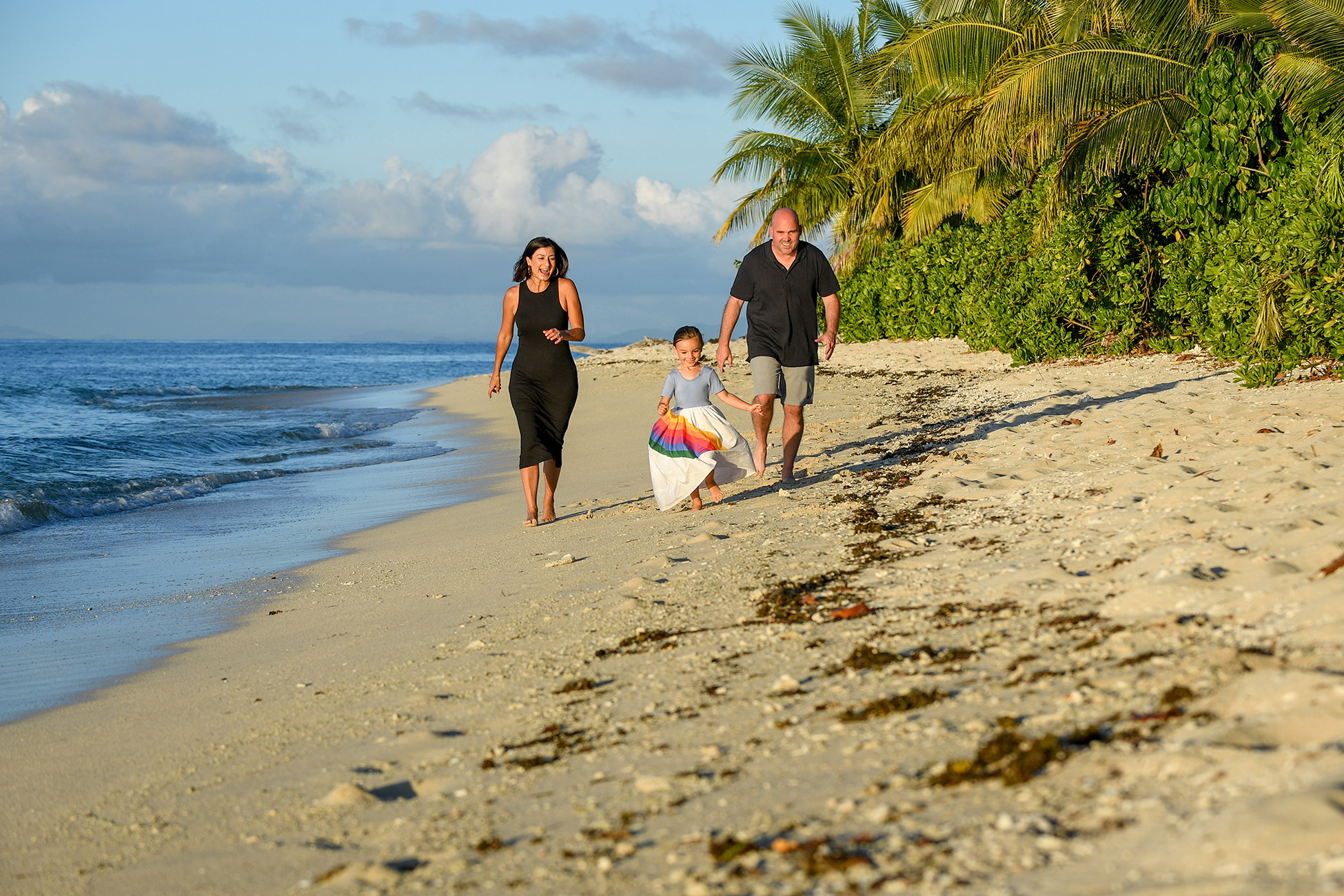 Father, mother and daughter run on the beach