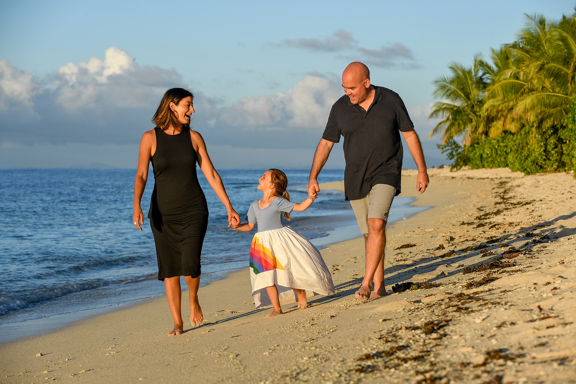 The cute family holds hands as they stroll on the beach