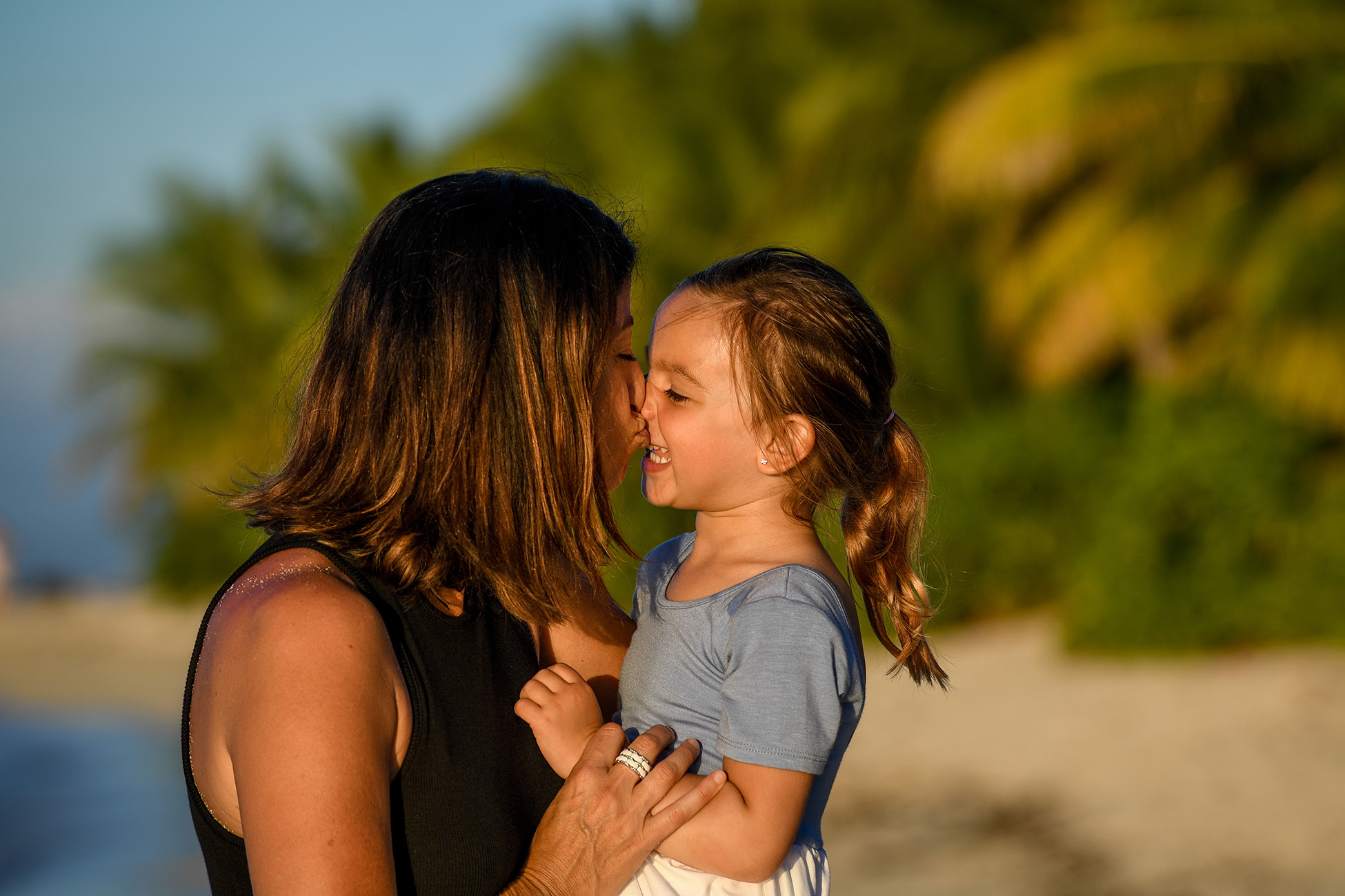 A mother kisses her daughter while on the beach