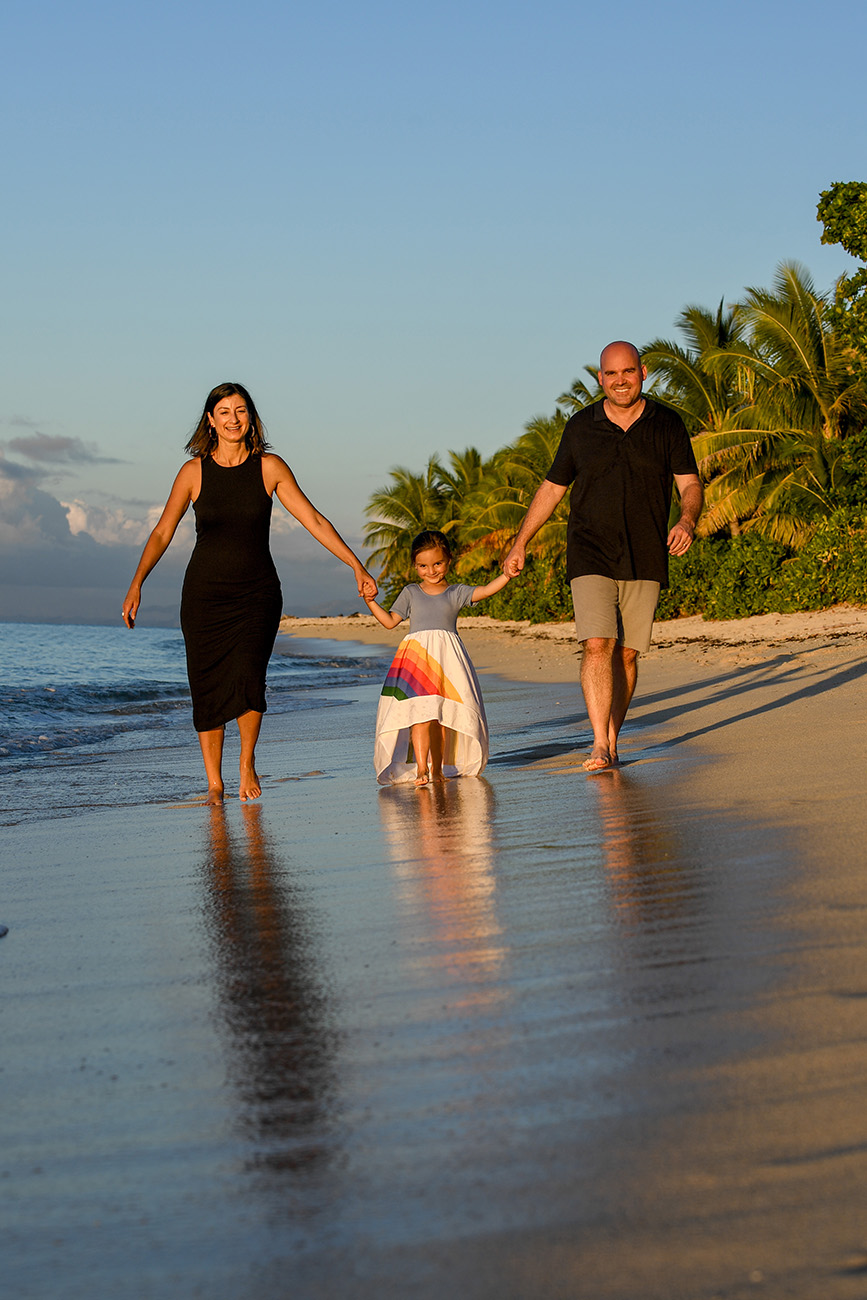 The sun kissed family hold hands as they wade in shallow waters at sunset