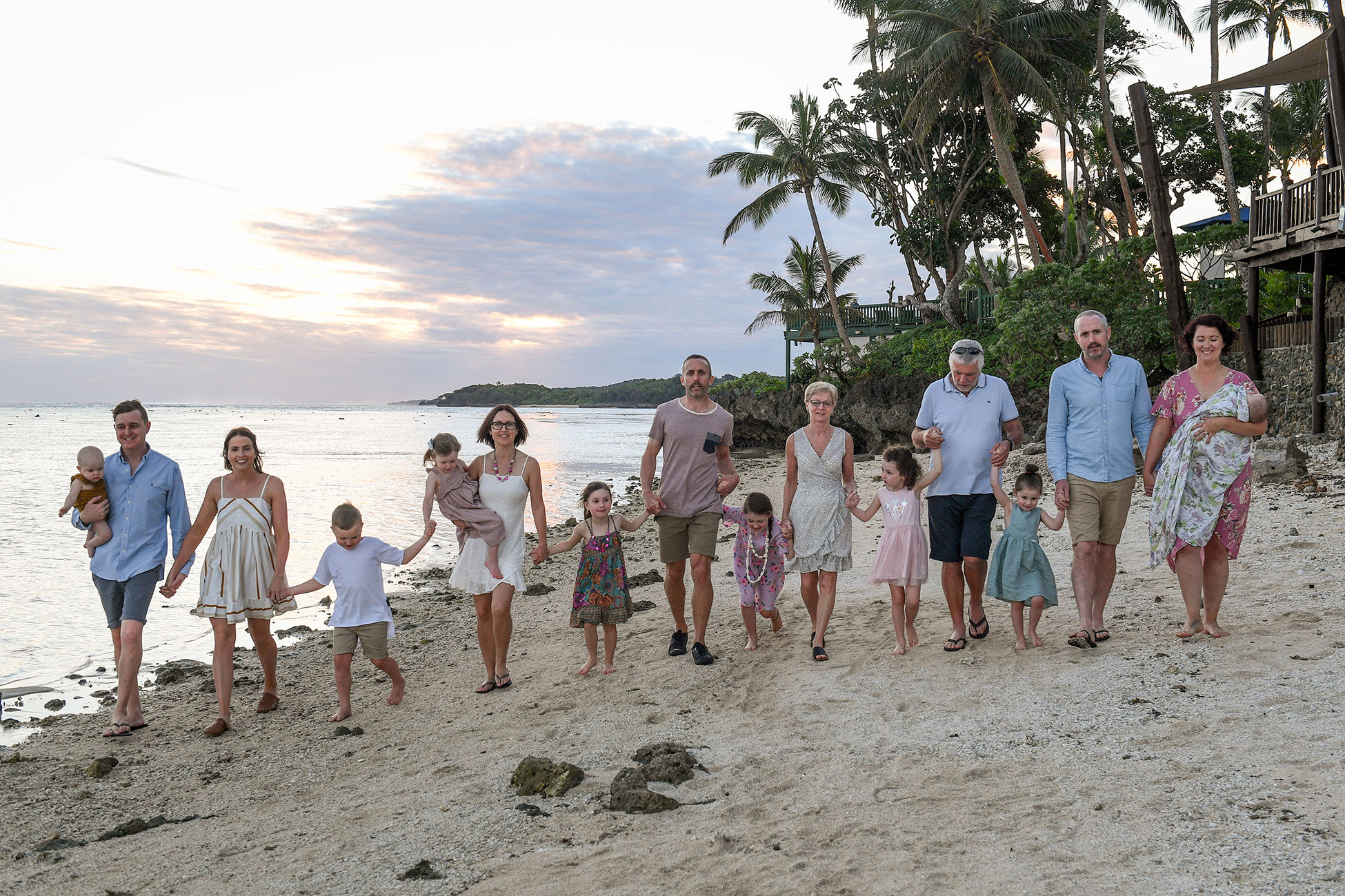 Group shot of the whole family walking together hands in hands on the beach of the Shangri La in Fiji at sunset.